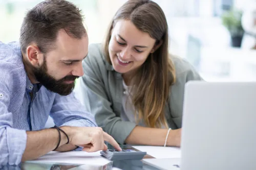 Casal a calcular valores com uma calculadora e portátil sobre a mesa